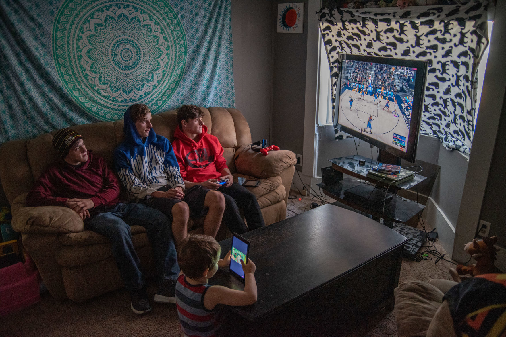 From left, Tyler Beck, Cody Beck and Taylor Beck play video games while TaylorÕs nephew Landon Michael Scott Beck, 4, watches a video on his tablet in the living room on Sunday, November 10, 2019.